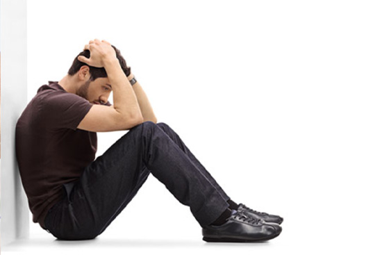 Man sitting on floor against a wall, with head in his hands